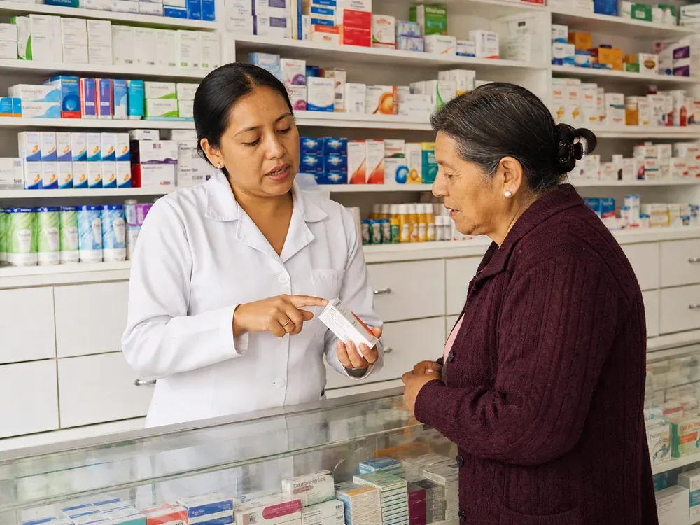 Farmacéutica explicando un medicamento a una clienta en el mostrador